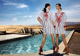 The image features two models standing back-to-back by a shimmering pool, set against a backdrop of vast desert dunes. They are wearing stylish, oversized striped shirts adorned with striking red embroidery. Their outfits are complemented by bold red high-heeled sandals. The scene captures a blend of fashion and nature, illuminated by bright sunlight, with clear blue skies and a feel of luxury and elegance. The brand name "Maryan Mehlhorn" is displayed prominently in the corner.