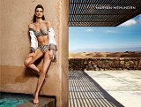 L'image montre un modèle posant dans un cadre extérieur stylisé. Elle porte un maillot de bain à pois, associé à une veste légère. Son expression est élégante et confiante. L'arrière-plan présente un paysage désertique avec des dunes, tandis que des ombres se dessinent sur le sol, créant un effet graphique intéressant. Le nom "MARYAN MEHLHORN" est affiché dans le coin supérieur droit, indiquant la marque. L'ensemble de la composition évoque une atmosphère sophistiquée et estivale.